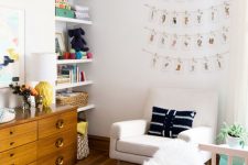 a pretty and cozy neutral nursery with open built-in shelves, a stained credenza for storage, a creamy chair, a white crib and printed textiles