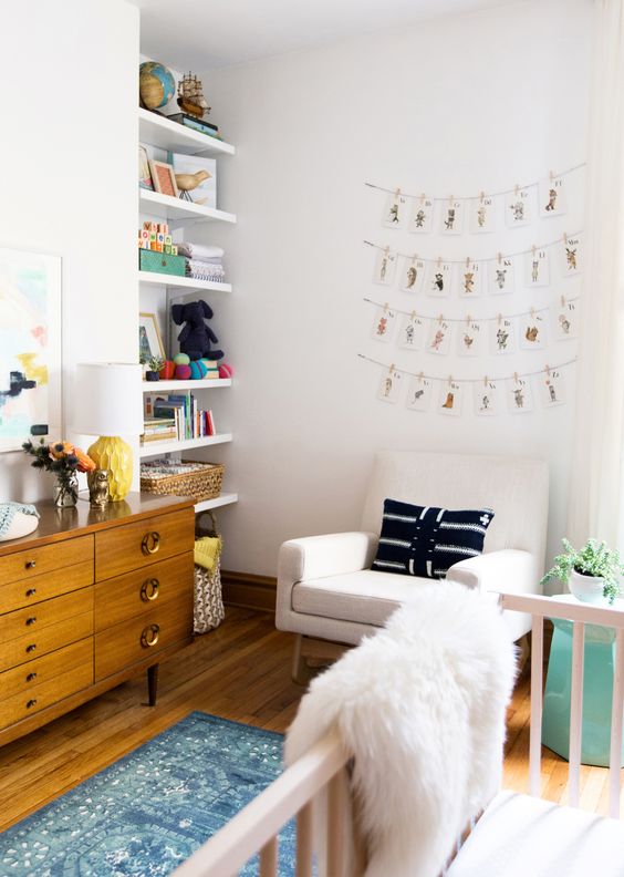 a pretty and cozy neutral nursery with open built-in shelves, a stained credenza for storage, a creamy chair, a white crib and printed textiles