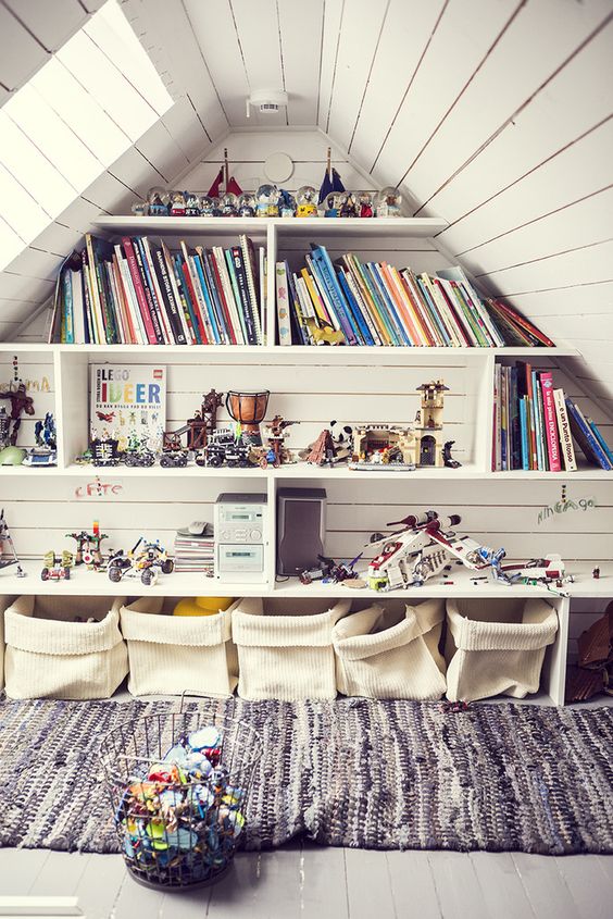 a pretty attic space turned into a kids' playroom with built-in shelves, storage bags and a rug plus lots of toys everywhere
