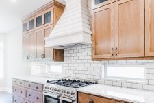 a rustic kitchen with light-stained shaker style cabinets, a white subway tile backsplash and white stone countertops, a white wood clad hood