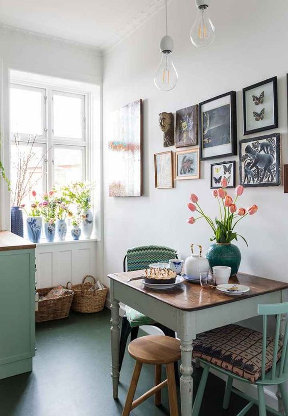 a small dining space with an aqua dining table, mismatching vintage and industrial chairs, a wooden stool and a bright gallery wall