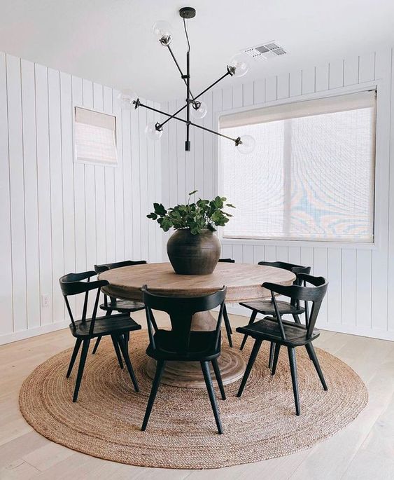 a stylish and contrasting dining room with a jute rug, a stained table and black chairs, a black chandelier and a potted plant