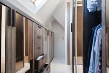a stylish and light-filled attic closet with well-organized wardrobes with ,oving doors and a cool storage unit with drawers and mirrors
