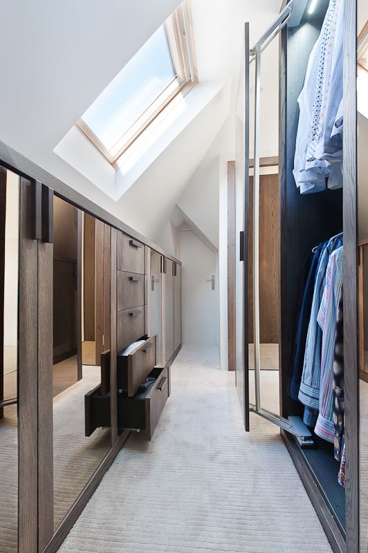 a stylish and light-filled attic closet with well-organized wardrobes with ,oving doors and a cool storage unit with drawers and mirrors