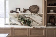 a stylish and luxurious kitchen with stained cabinets, a white marble backsplash and countertops and a window that floods the space with naturla light