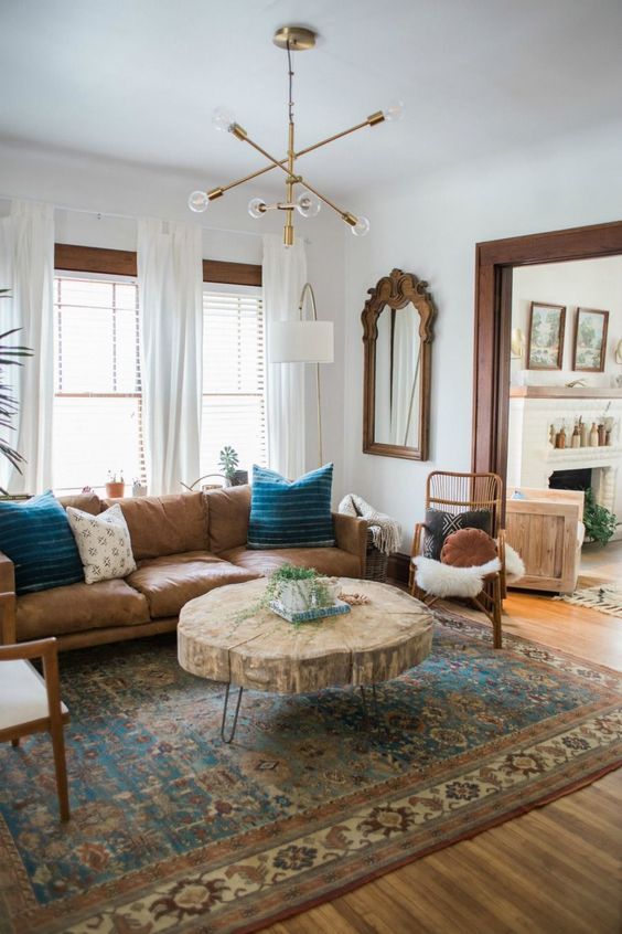 a stylish farmhouse living room with a modern brown leather sofa, a rustic living edge table with hairpin legs, rattan chairs and a mirror in a wooden frame plus a boho rug