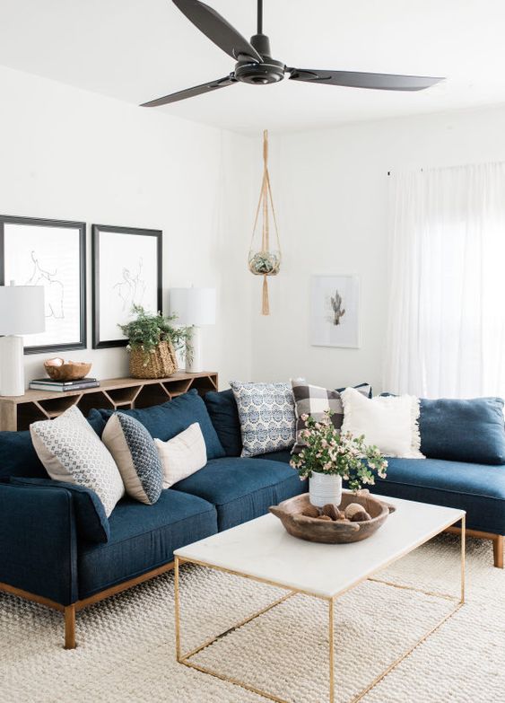 a stylish mid-century modern neutral living room with a navy sectional, a coffee table, a lovely credenza, some pretty artwork and potted greenery and blooms