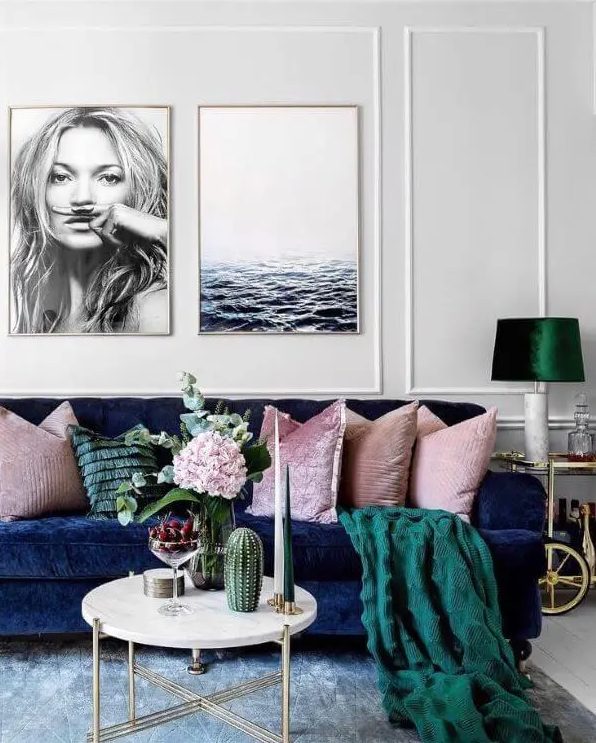 a welcoming living room with a navy sofa, pink pillows and a green blanket, a lamp with an emerald lampshade, a round coffee table and some blooms