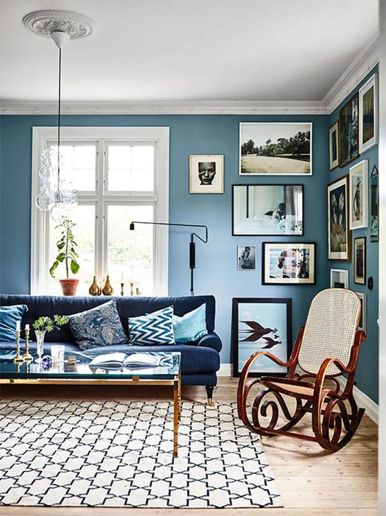 a welcoming living room with dusty blue walls, a creative gallery wall, a navy sofa, a glass coffee table and a rocker chair