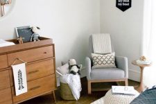 a welcoming mid-century modern nursery in neutrals, with a grey rocker, a stained dresser, a white crib, a white pouf, baskets with toys and printed textiles