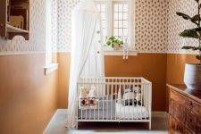 a welcoming mid-century modern nursery with printed wallpaper and rust walls, a vintage stained dresser, a white crib, neutral textiles, an open shelf