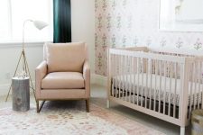 a welcoming neutral mid-century modern nursery with a tan crib, a tan chair, printed layered rugs, printed wallpaper, dark green curtains, a side table