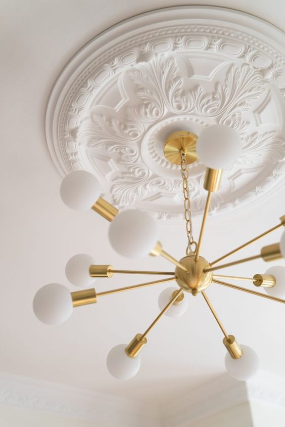 a white ceiling medallion with a gold sunburst chandelier - the vintage look of the medallion and modern look of the chandelier contrast