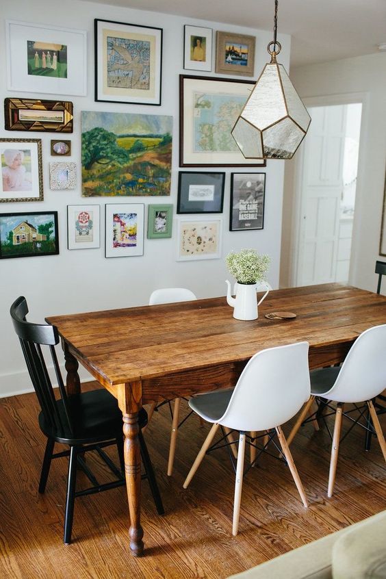 an eclectic dining room with a vintage stained dining table, white Scandinavian chairs, a vintage black chair and a bright gallery wall