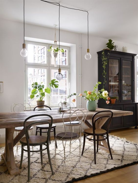 an eclectic dining space with a rustic trestle dining table, mismatching vintage and modern chairs, hanging bulbs