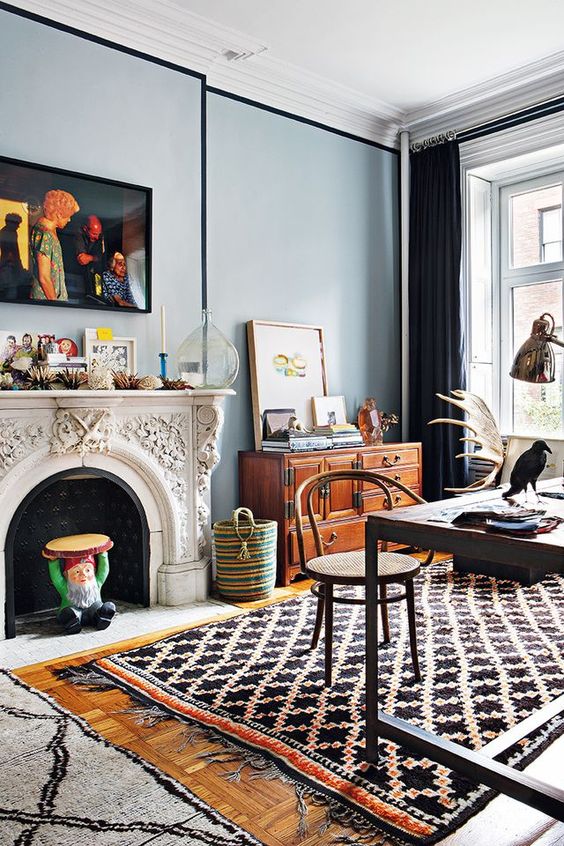 an eclectic space with a vintage non working fireplace, a large industrial dining table, a vintage stained file cabinet, layered rugs, artworks and books