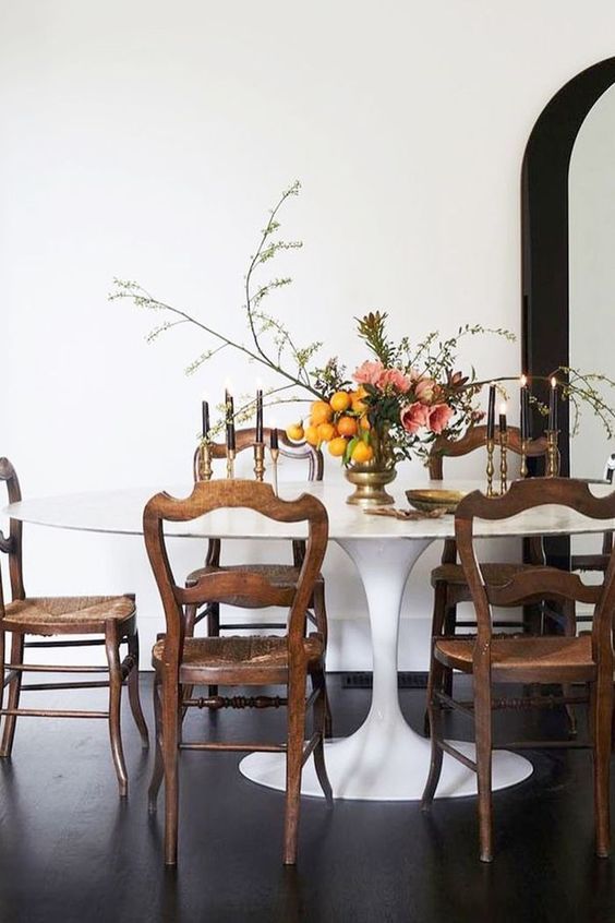 an elegant dining room with a large oval dining table, vintage stained chairs, an arched mirror in a black frame and blooms