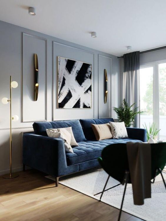 an elegant living room with dove grye walls, a navy sofa, a black chair, a chic artwork and some gold and brass touches for a chic look
