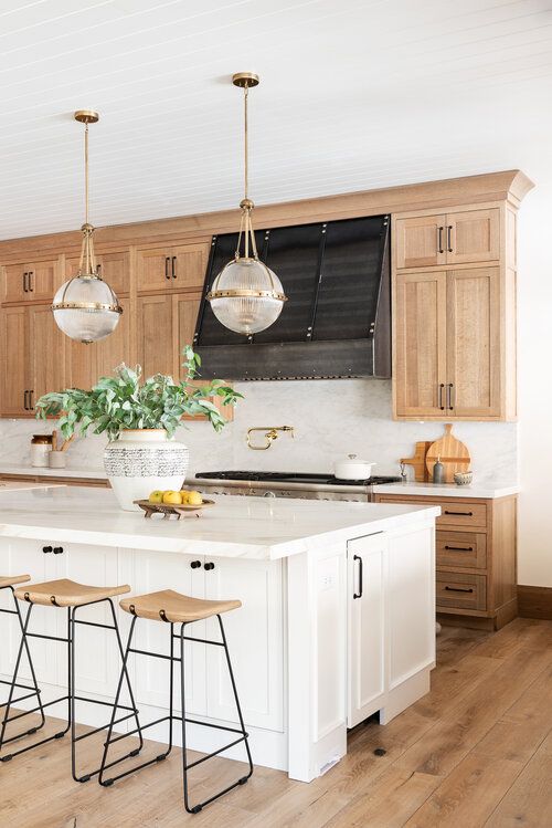 an inviting farmhouse kitchen with light stained shaker style cabinets, white stone countertops and a white backsplash, wooden stools and a white kitchen island