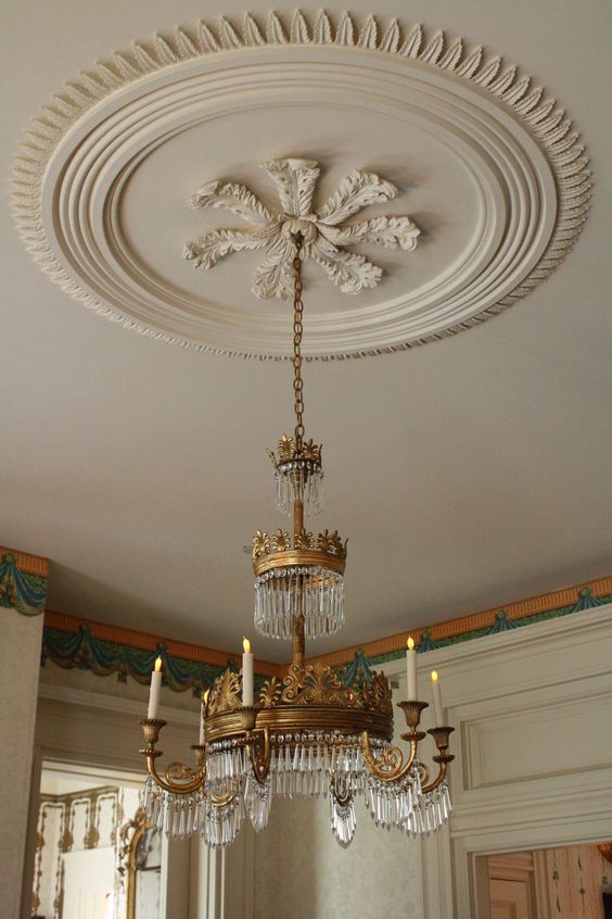 an oversized refined off-white ceiling medallion that matches the color of the ceiling and a whimsical crystal and gold chandelier with candles