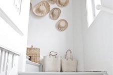 03 a clean white space fets a beach and relaxed feel with a gallery wall of hats and some canvas and straw bags on the floor