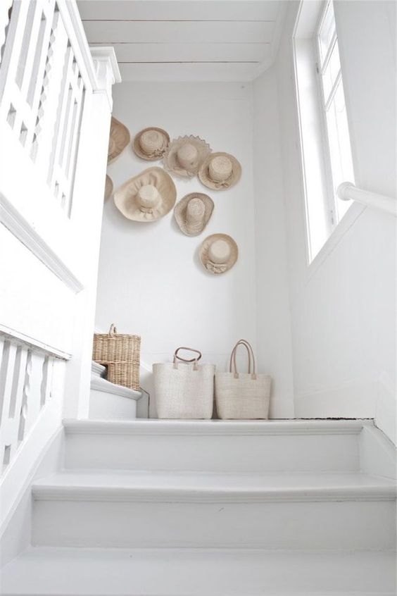 a clean white space fets a beach and relaxed feel with a gallery wall of hats and some canvas and straw bags on the floor