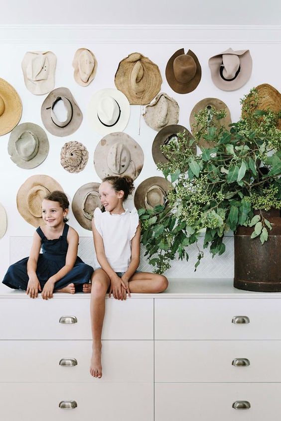 a large dresser with greenery and a whole wall over it that shows off all the possible hats of the family