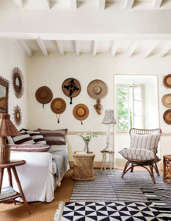 a Mediterranean space with neutral decor, wooden and rattan items, hats on the wall that add coziness and interest to the space