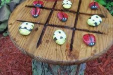 10 a tree stump with a wooden plate with bright bugs of pebbles is a cool tic-tac-toe idea for a garden