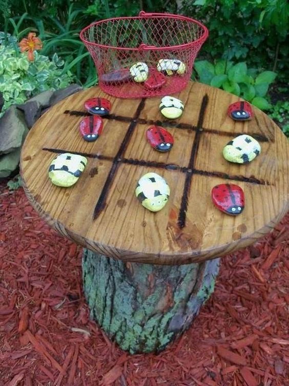 a tree stump with a wooden plate with bright bugs of pebbles is a cool tic-tac-toe idea for a garden