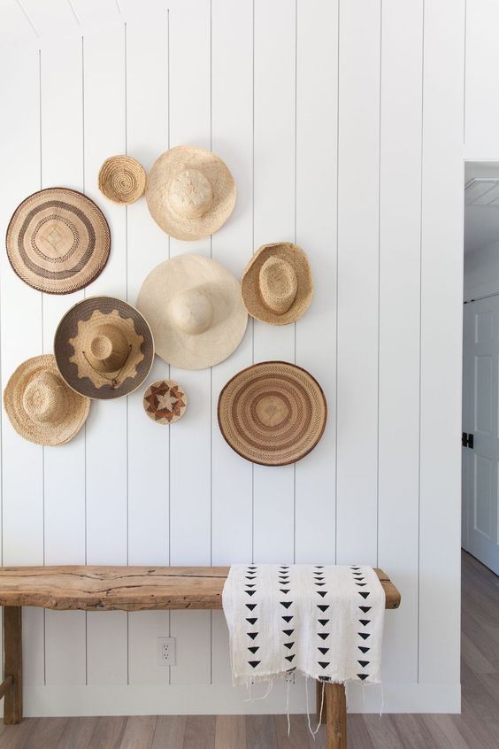 a neutral rustic entryway with a wooden bench, a printed blanket, a gallery wall of hats used instead of baskets for a cozy and warm feel