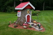 14 a small tree stump elf house with a red roof and windows, a red door and some blooms and gnome figurines is amazing