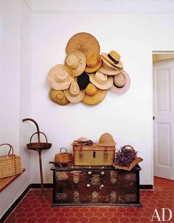 a vintage rustic entryway with chests, straw bags and a holder with lots of straw hats - they cover the holder easily