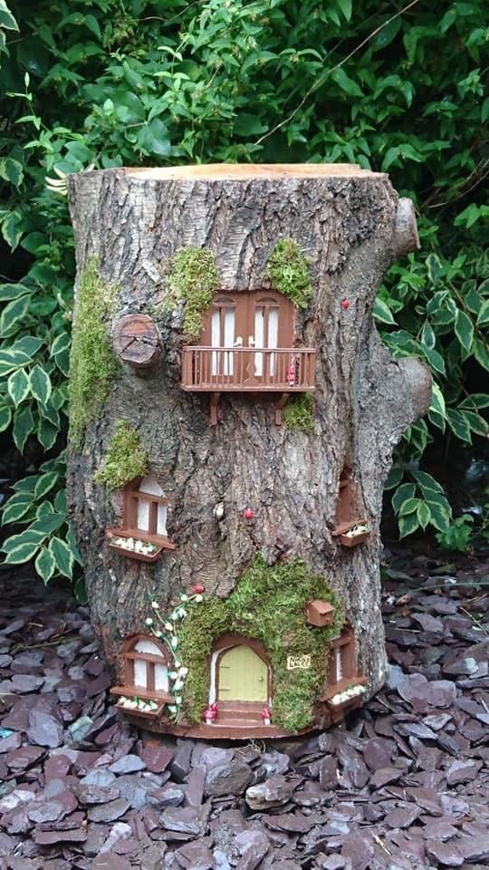 a tree stump turned into a whimsy decoration with windows and doors, with moss and blooms is a peculiar piece for a garden
