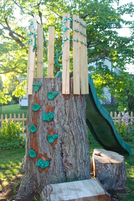 a climbing wall play set of a large tree stump, a slider and some wood and rope is a cool idea for a rustic outdoor space