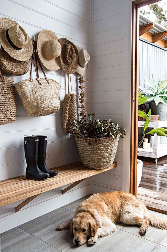 a lovely rustic entryway with a wall-mounted wooden bench, a basket with greenery and a holder with hooks that allows you display straw hats and bags