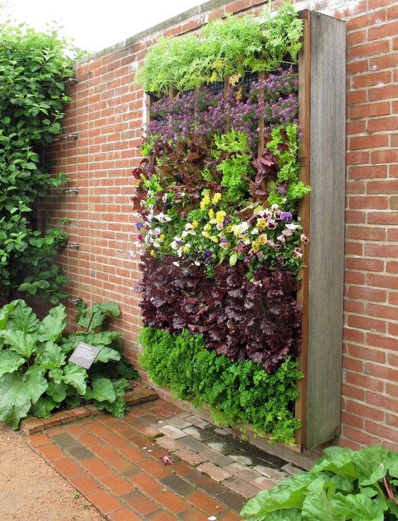a wall-mounted vertical garden of wood and metal, with lots of blooms and herbs is a lovely idea for a small outdoor area