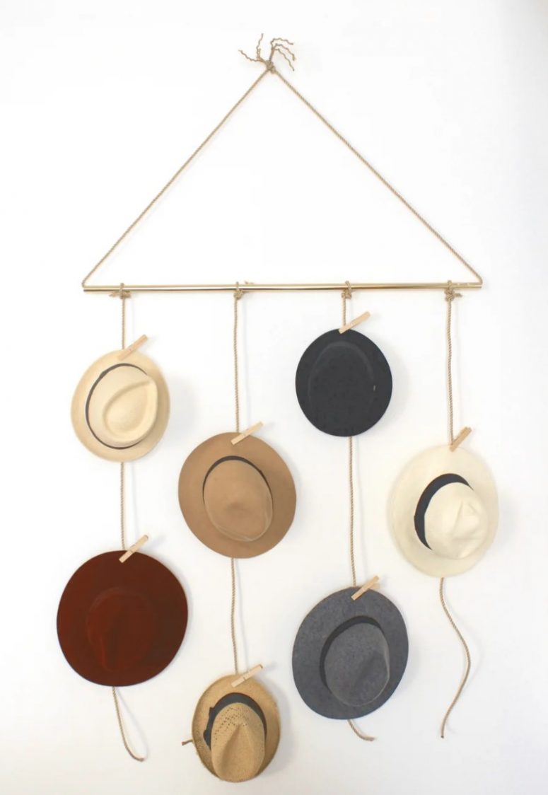 a pretty and simple hat holder of rope and a gold tube, with hats hanging on the rope and clothes pins is an easy piece that can be DIYed