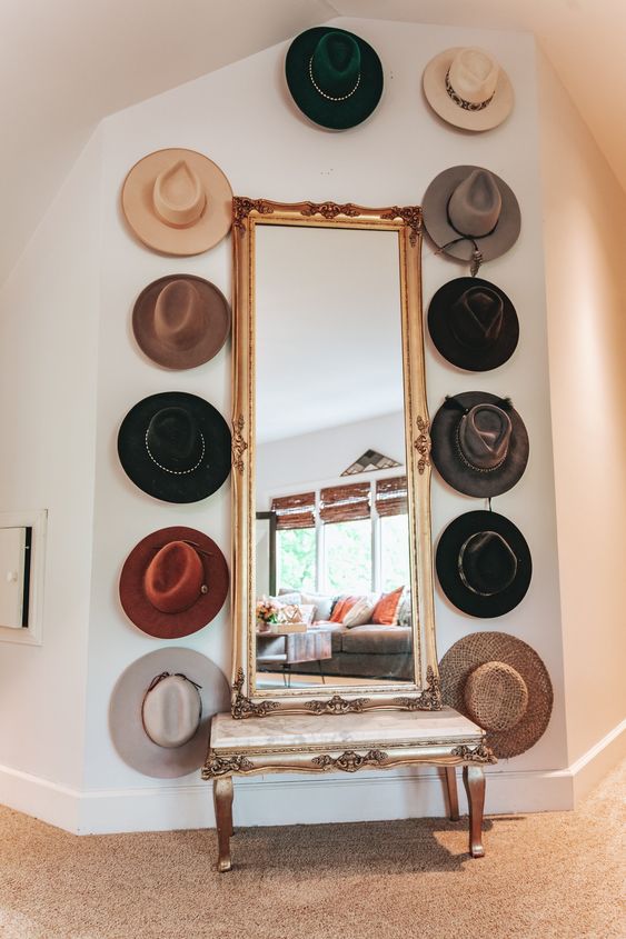 a vintage inspired nook with a large mirror in a frame, a refined bench and hats placed around the mirror is a very cool idea