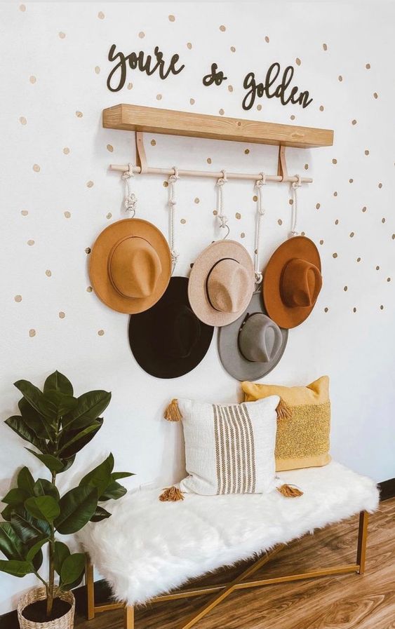 a welcoming entryway with a gilded bench with faux fur, neutral pillows, a rack with ropes with hooks to hang all the hats, calligraphy decor and potted plants