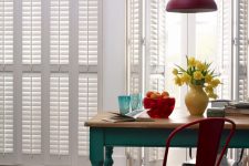 French doors covered with plantation shutters here look neat and blend seamlessly into a white kitchen here creating a cool backdrop for bright furniture