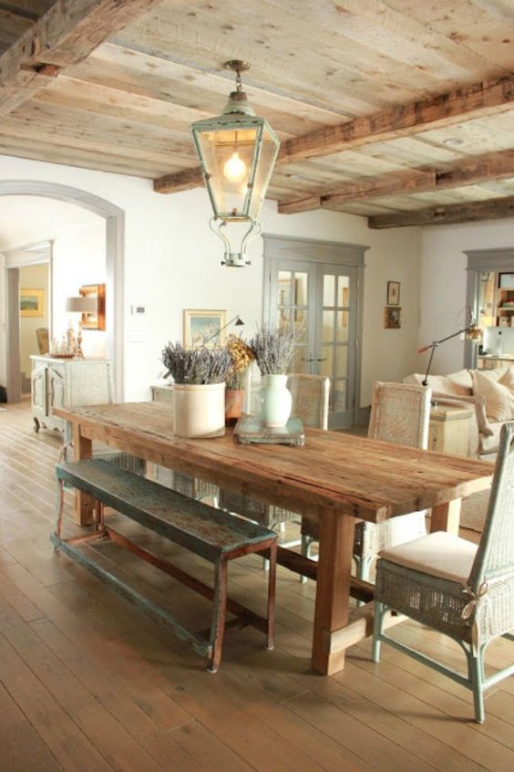 a French chic dining space clad with wood, with a stained table, benches and chairs, a candle lantern and some lavender in vases