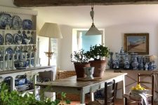 a French chic dining room with a buffet with blue porcelain, a rustic dining table, stained chairs and pendant lamps and baskets