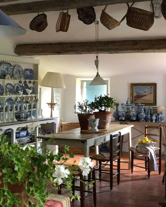 a French chic dining room with a buffet with blue porcelain, a rustic dining table, stained chairs and pendant lamps and baskets