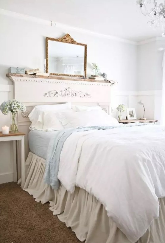 a French country bedroom with white paneling, a bed with a refined headboard, blue and white bedding, books and a mirror, a crystal chandelier