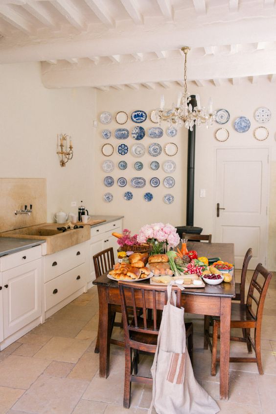 a Provence dining room with white cabinetry, a stained dining table and chairs, a vintage hearth, a gallery wall of blue plates