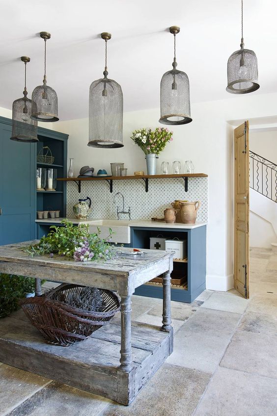a beautiful French chic kitchen with sleek navy cabinetry, a shabby chic kitchen island, pendant lamps and greenery and blooms