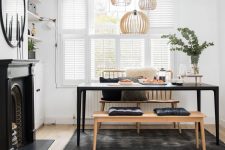 a beautiful Scandinavian dining room with tier on tier shutters, built-in shelves and a cabinet, a non-working fireplace, a black table and benches