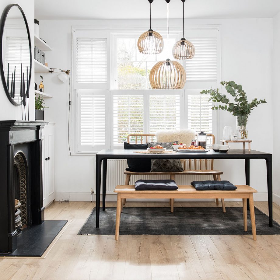 a beautiful Scandinavian dining room with tier on tier shutters, built in shelves and a cabinet, a non working fireplace, a black table and benches