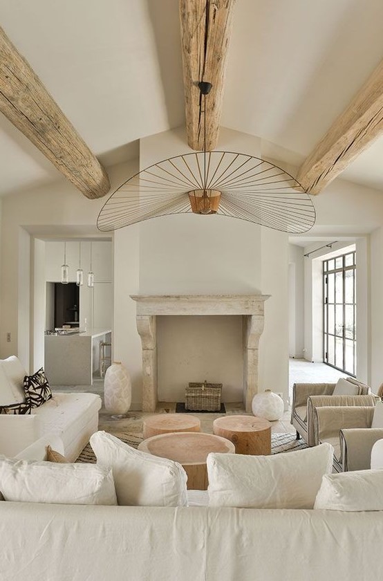 a beautiful neutral living room with wooden beams, a fireplace, neutral furniture, tree stumps as coffee tables